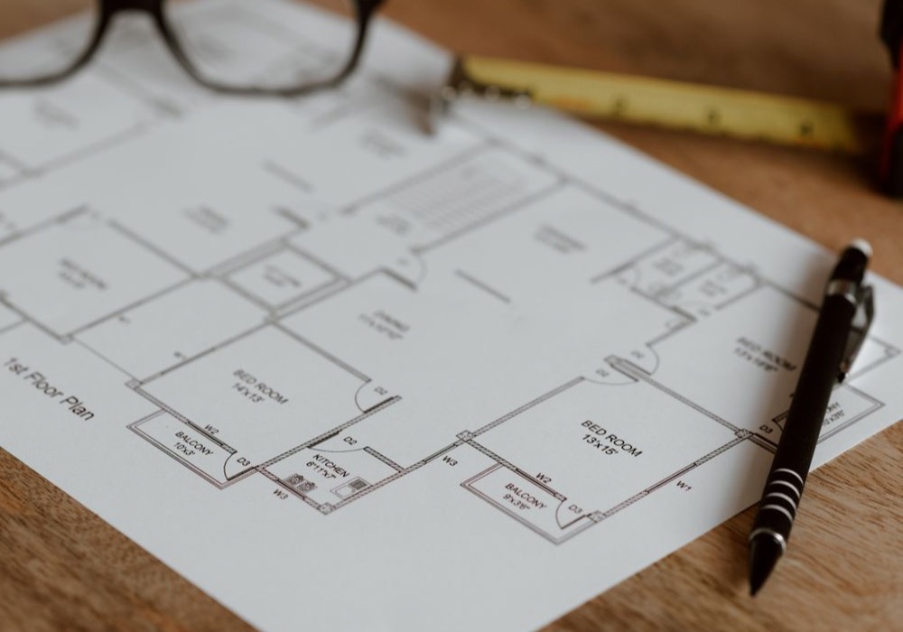 Plan d’un logement annoté au crayon, posé sur un bureau avec un mètre ruban